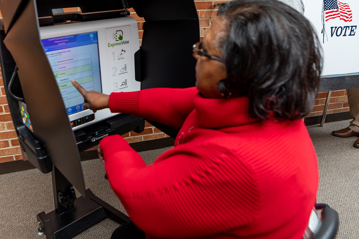 A seated voter using the ExpressVote with kiosk in the lowered position and privacy blinds