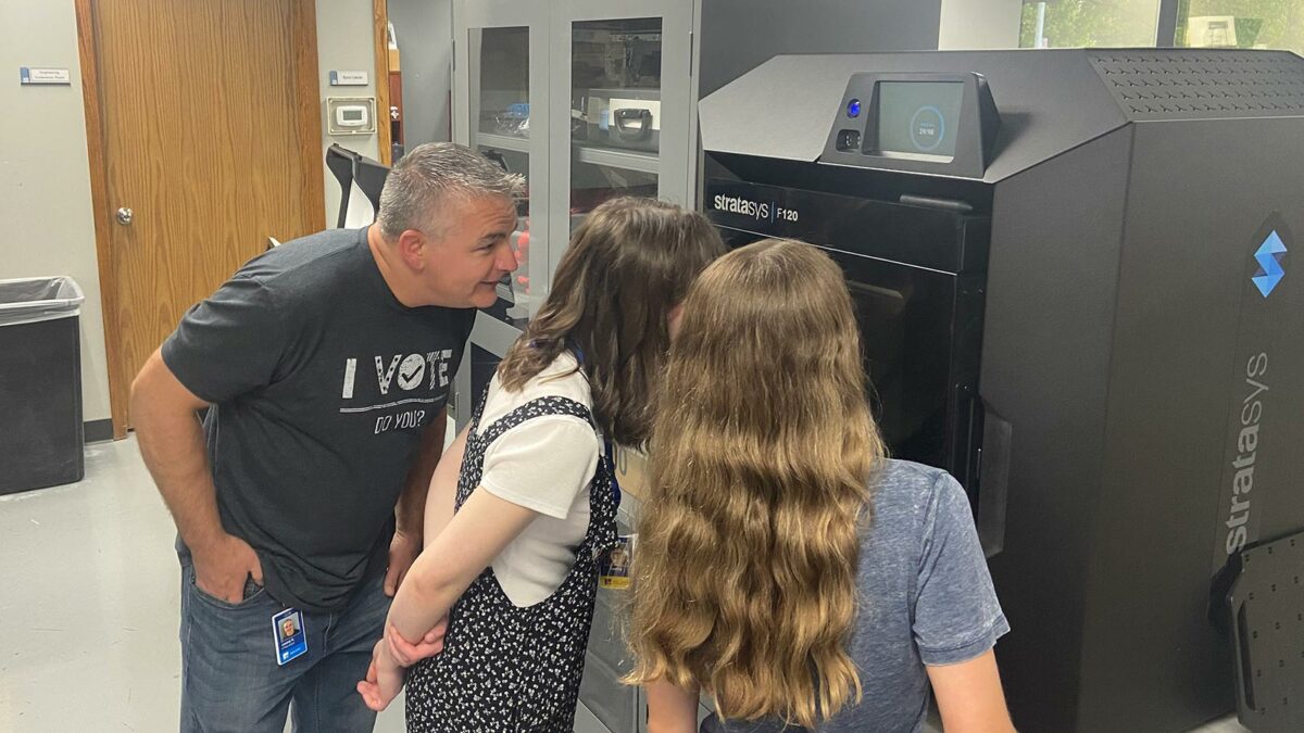 Two girls and one dad looking into a 3D printer.